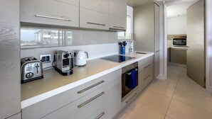 A modern kitchen with a built-in oven, a coffee maker, and a toaster. There is a sink and a window overlooking the street. - Le Paradis Penthouse Apartment (Hermanus)