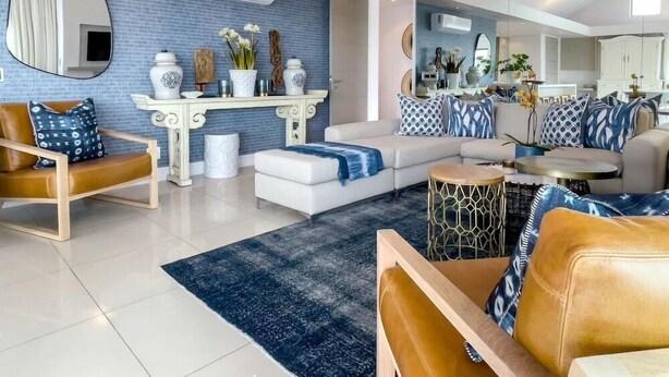 A modern living room with a blue brick wall, white furniture, and a large mirror reflecting the space. - Le Paradis Penthouse Apartment (Hermanus)