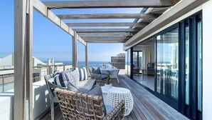 A balcony with wicker furniture, a glass table, and a white round table. - Le Paradis Penthouse Apartment (Hermanus)