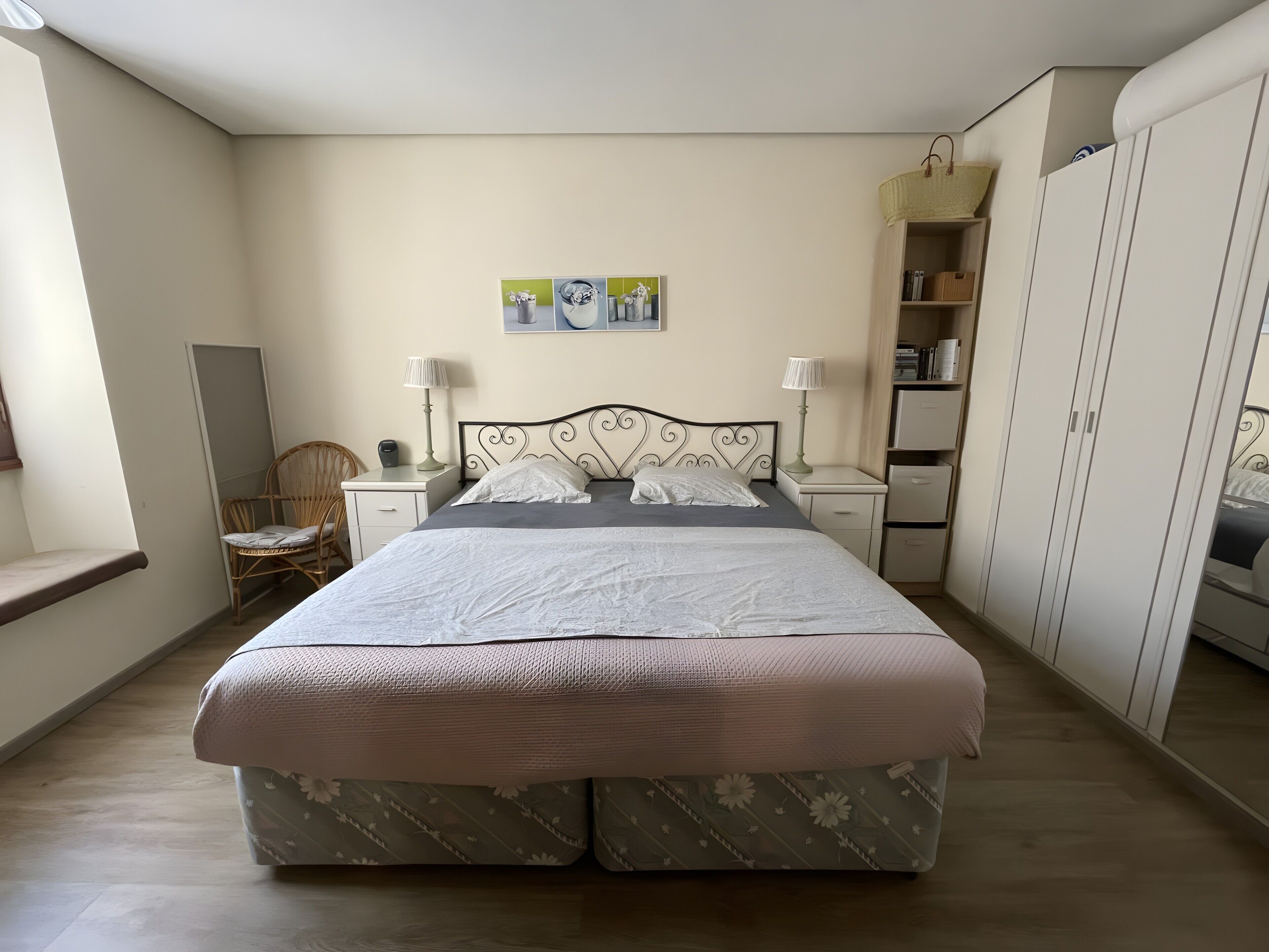Un dormitorio con cama, mesitas de noche, una silla, armario y estante en la pared.