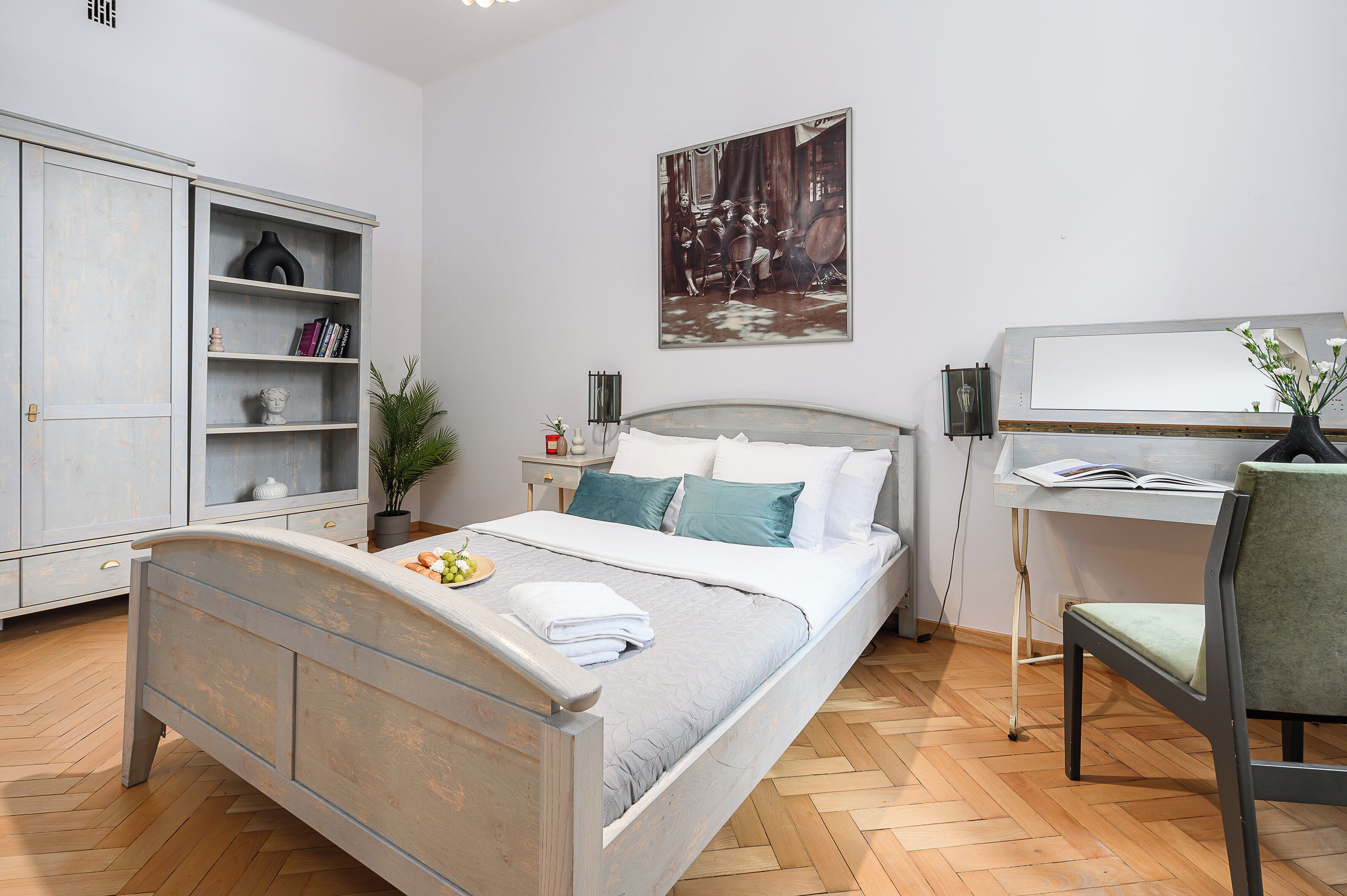 A bedroom with a bed, a desk, a chair, a wardrobe, and a painting on the wall.