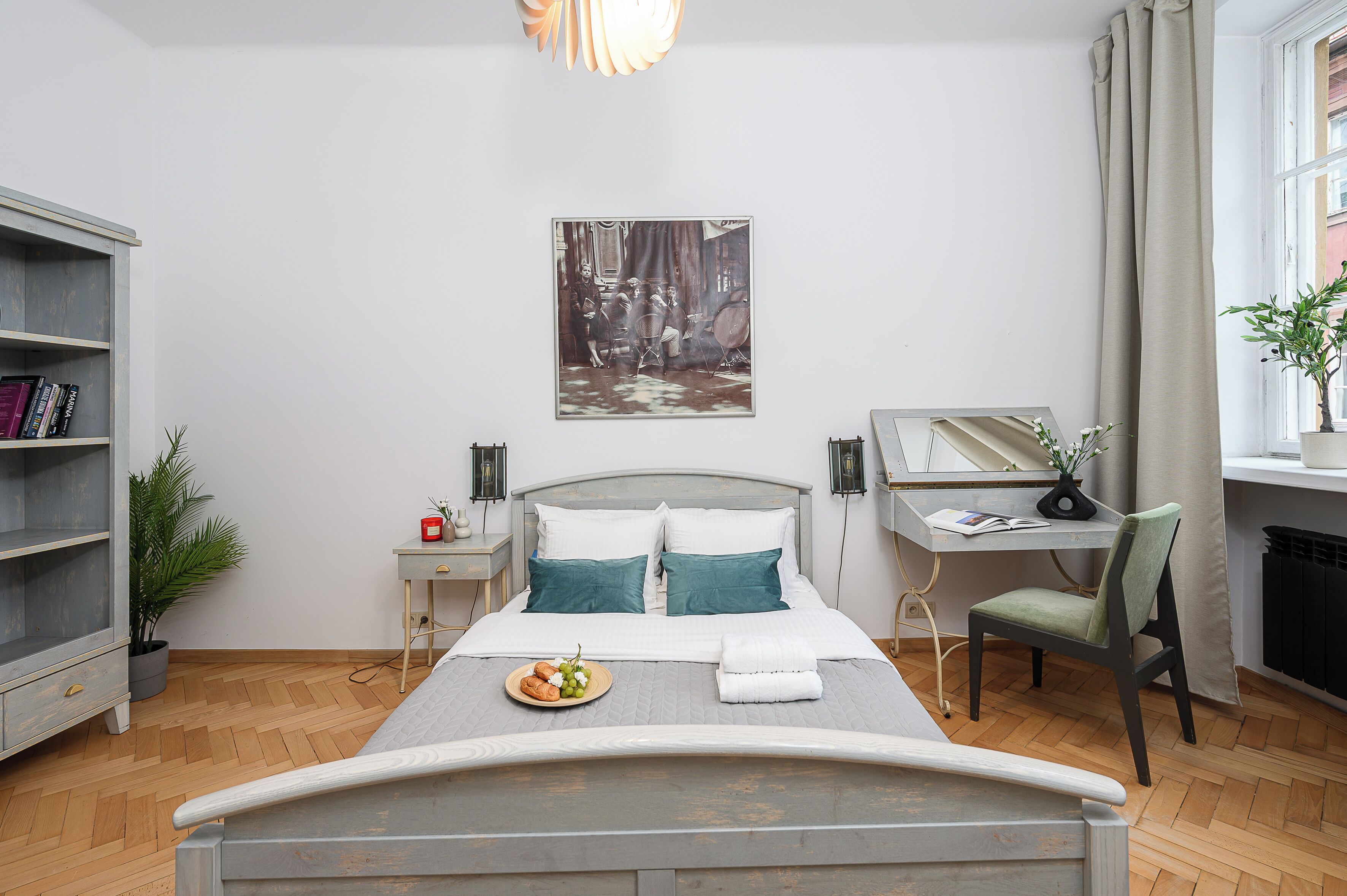 A neatly arranged bedroom with a bed, bedside table, desk, chair, and a bookshelf.