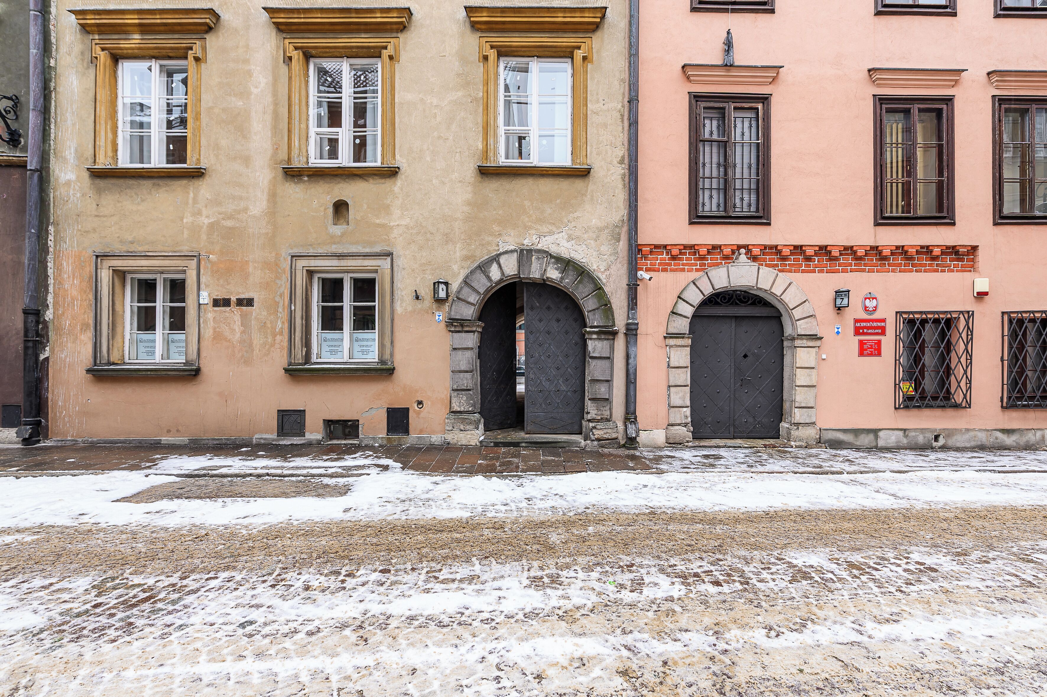 A building with multiple windows and doors, some with shutters, and a cobblestone ground.