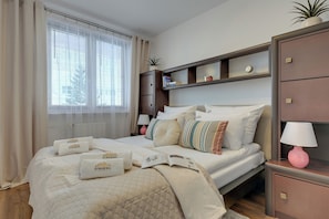 A neatly arranged bedroom with a bed, bedside tables, a nightstand, a shelf with books, and a window with curtains. - Piastowska near the Jelitkowo Beach & Reagan Park by Downtown Apartments (Gdańsk)