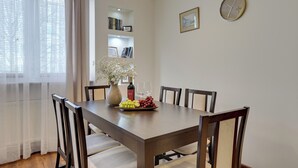 Un coin repas avec une table en bois, des chaises, un vase de fleurs, une bouteille et une assiette de fruits.