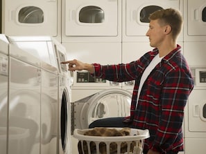 A person operating a front-loading washing machine in a laundromat with multiple machines.