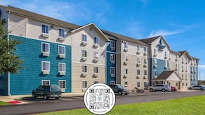 A multi-story hotel with a uniform exterior, air conditioning units, and a parking lot with cars.