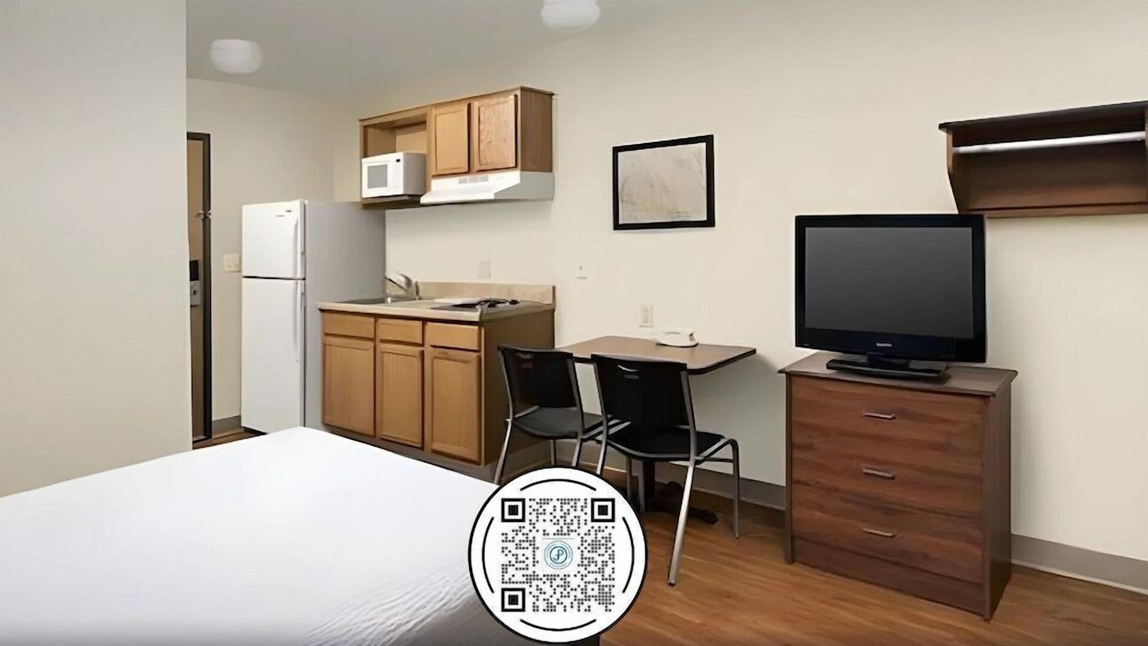 A compact room with a bed, a kitchenette, a TV, and a desk.