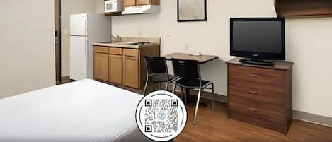 A compact room with a bed, a kitchenette, a TV, and a desk.
