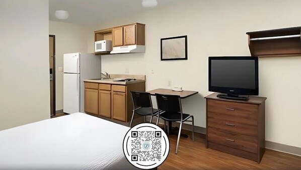 Una habitación pequeña con cama, kitchenette, televisor y escritorio.
