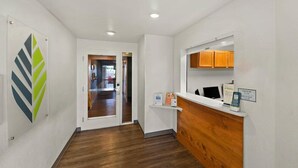 Un espace d’accueil comprenant un comptoir de réception en bois, un comptoir pour l’enregistrement des départs et une porte en verre donnant sur un couloir.