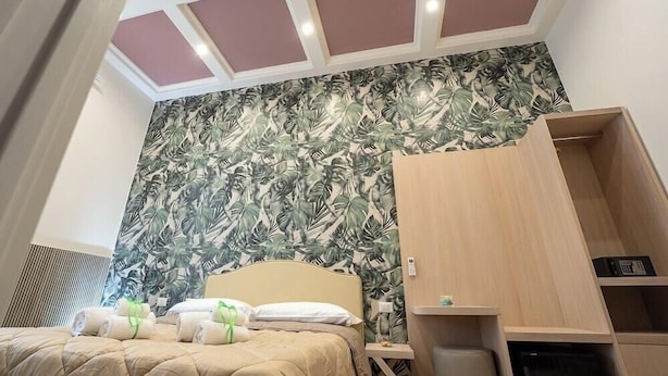 A hotel room with a bed, a wardrobe, a small table, and a wall with a tropical leaf pattern. - Naples Royal House B&B (Naples)