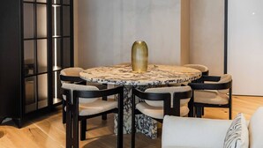 Mesa redonda com tampo de mármore e um vaso dourado, rodeada por quatro cadeiras com assentos acolchoados e estrutura preta.
