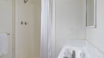 A bathroom with a shower, a toilet, and a sink with two faucets.