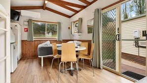 Une pièce chaleureuse avec un plafond en bois, une table à manger avec des chaises, un petit coin cuisine et une porte-fenêtre coulissante donnant sur l’extérieur.