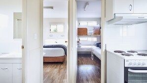 Une cuisine compacte équipée d’une cuisinière et de placards, une chambre avec un lit et une fenêtre, et une salle de bain avec des toilettes et un lavabo.