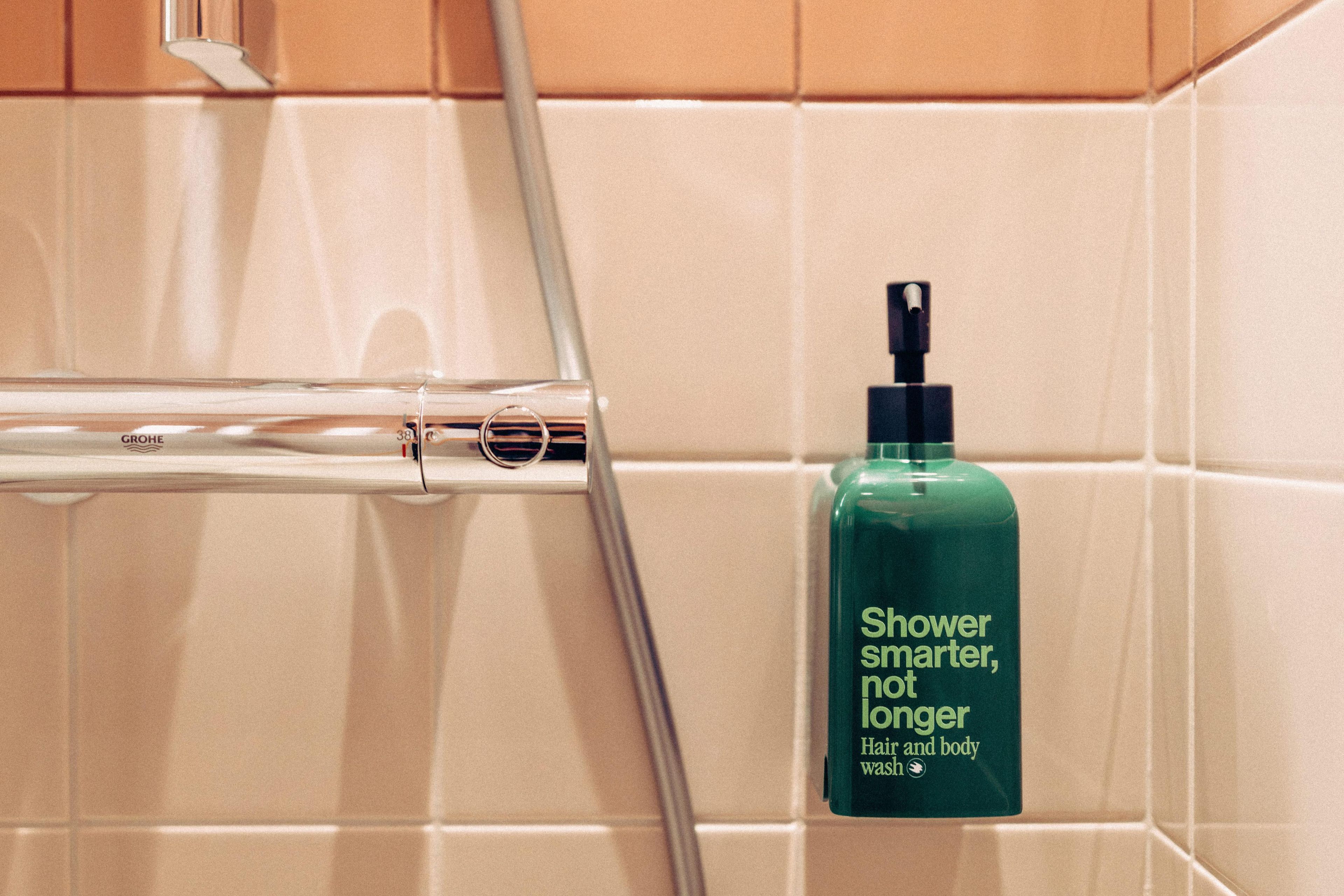 Un baño con ducha, secamanos y una botella de gel de baño Shower Smarter, Not Longer.
