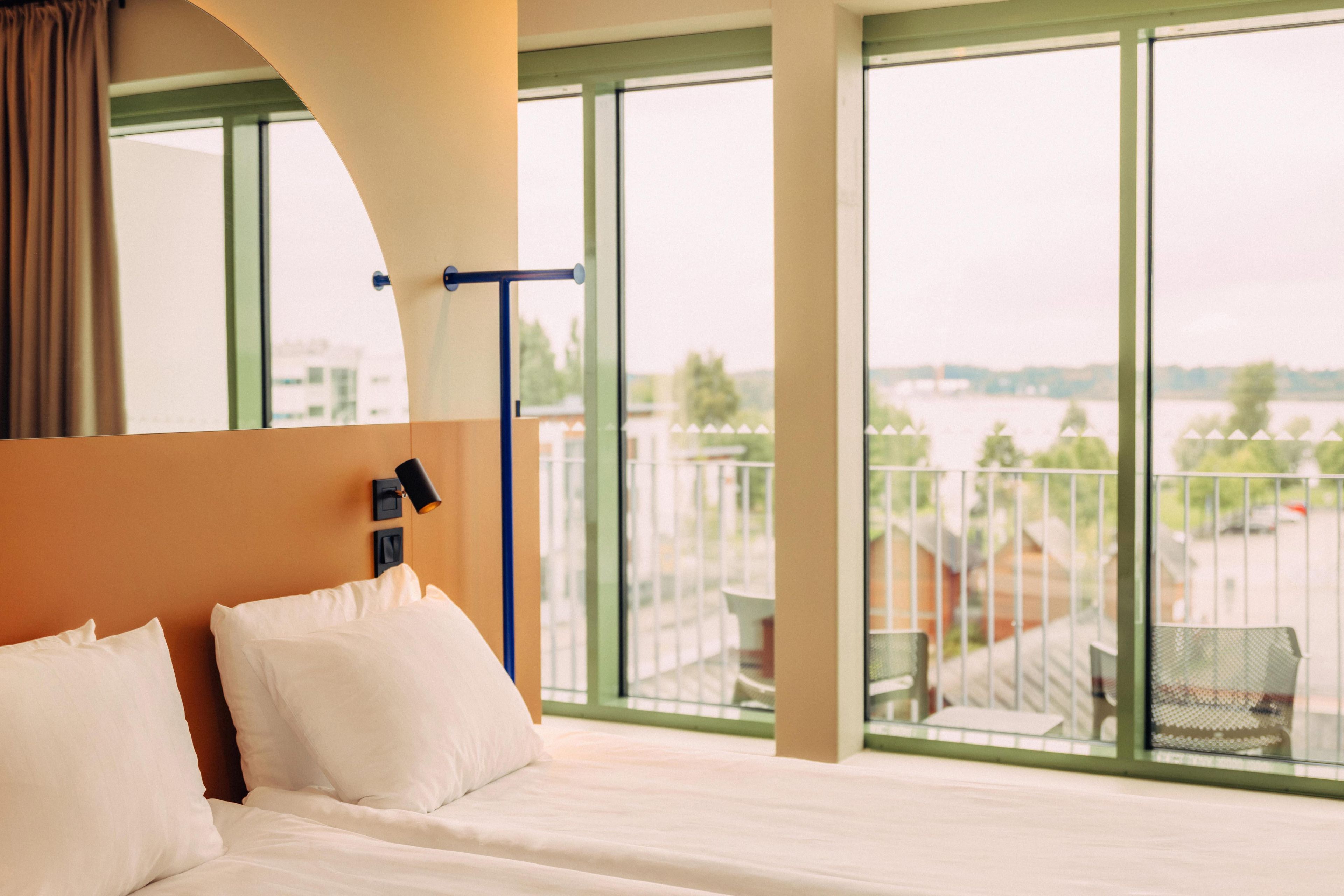 A hotel room with a large bed, a view of a balcony, and a window overlooking a body of water.