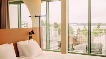 A hotel room with a large bed, a view of a balcony, and a window overlooking a body of water.