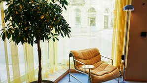 A room with a potted plant, a modern armchair, a floor lamp, and a view of a building through sheer curtains. - Scandic Go, Saaristonkatu 1 (Oulu)