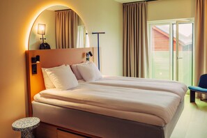 Uma cama de casal com cabeceira, uma mesa redonda pequena e uma cadeira em quarto de hotel com vista para o exterior.
