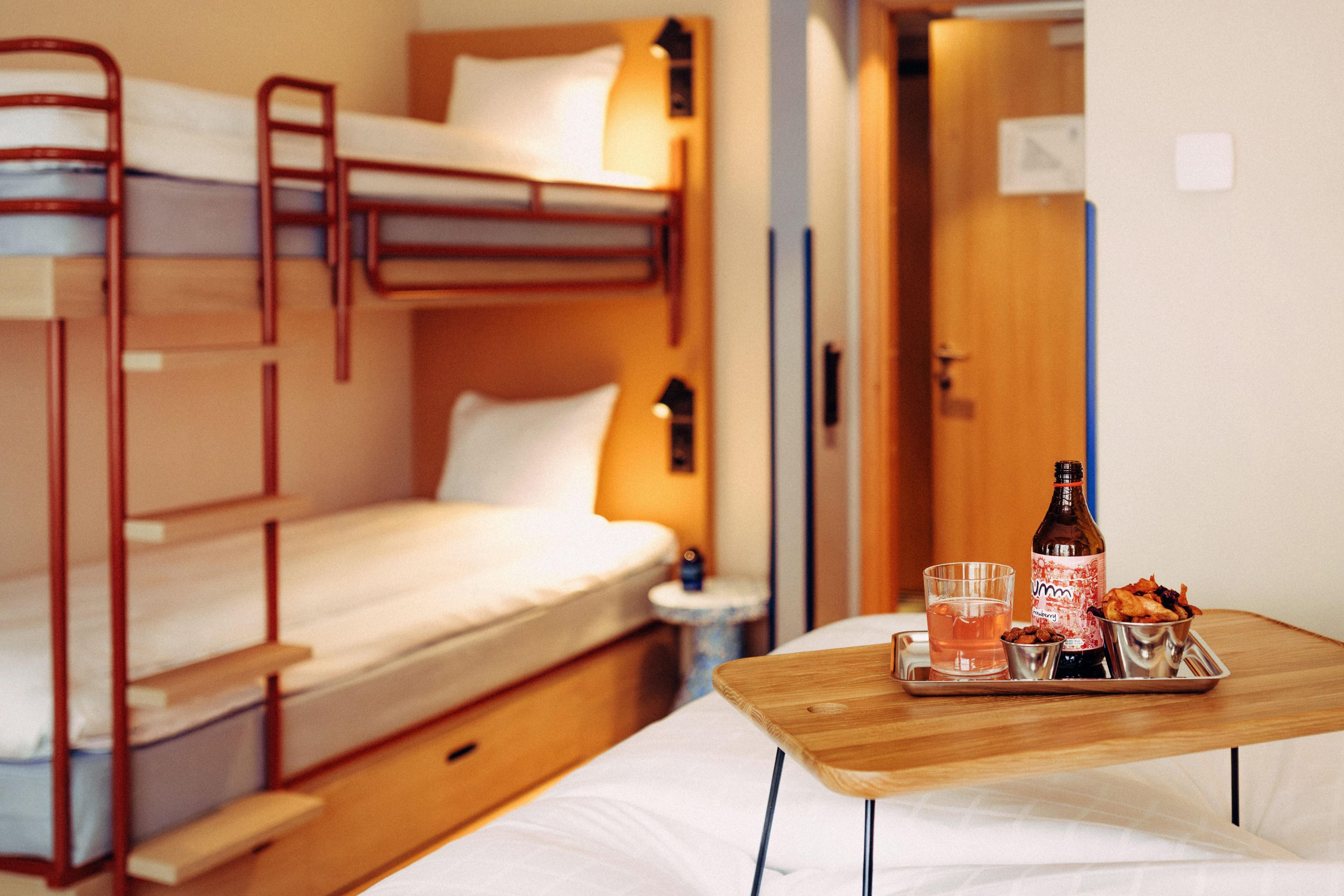 Une chambre avec un lit superposé, une table en bois, une bouteille et un plateau contenant de la nourriture et un verre.