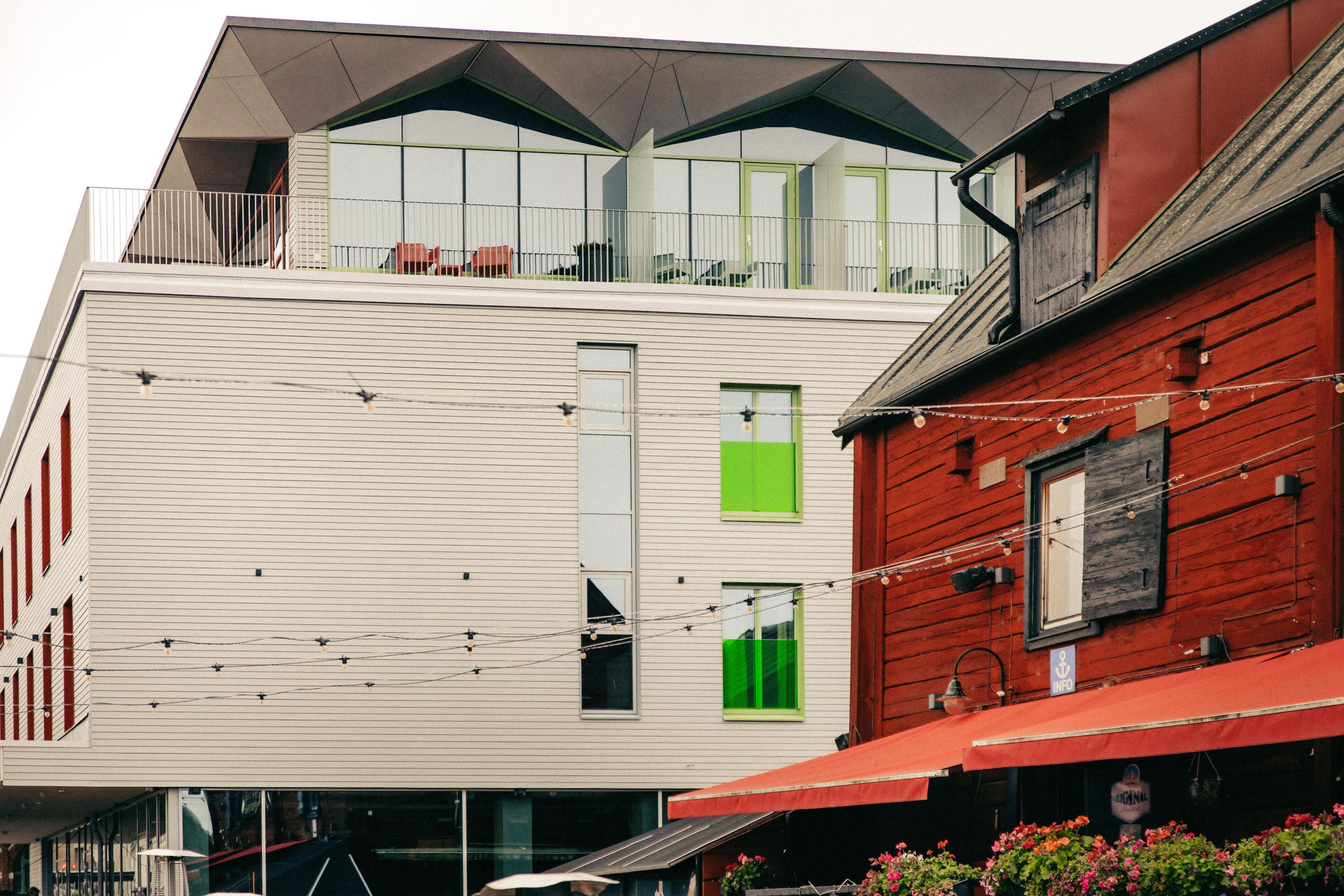 A multi-story building with a white facade and green windows, featuring balconies and a red wooden section.