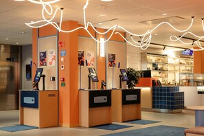 A reception area with three counters, each equipped with a digital kiosk and a small plant.
