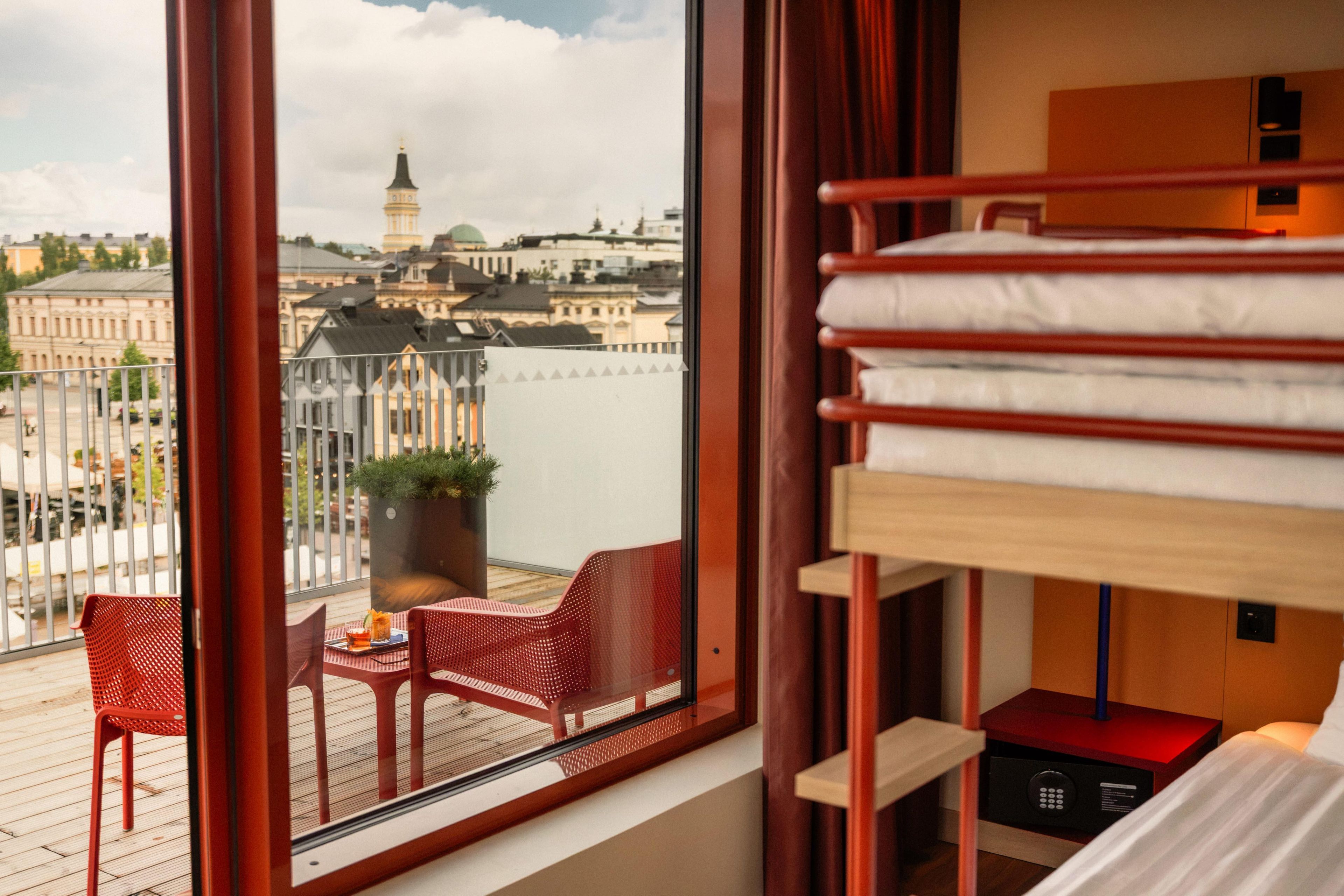 Ein Hotelzimmer mit großem Fenster, einem Etagenbett, einem kleinen Tisch mit Stuhl und einem Blumentopf.