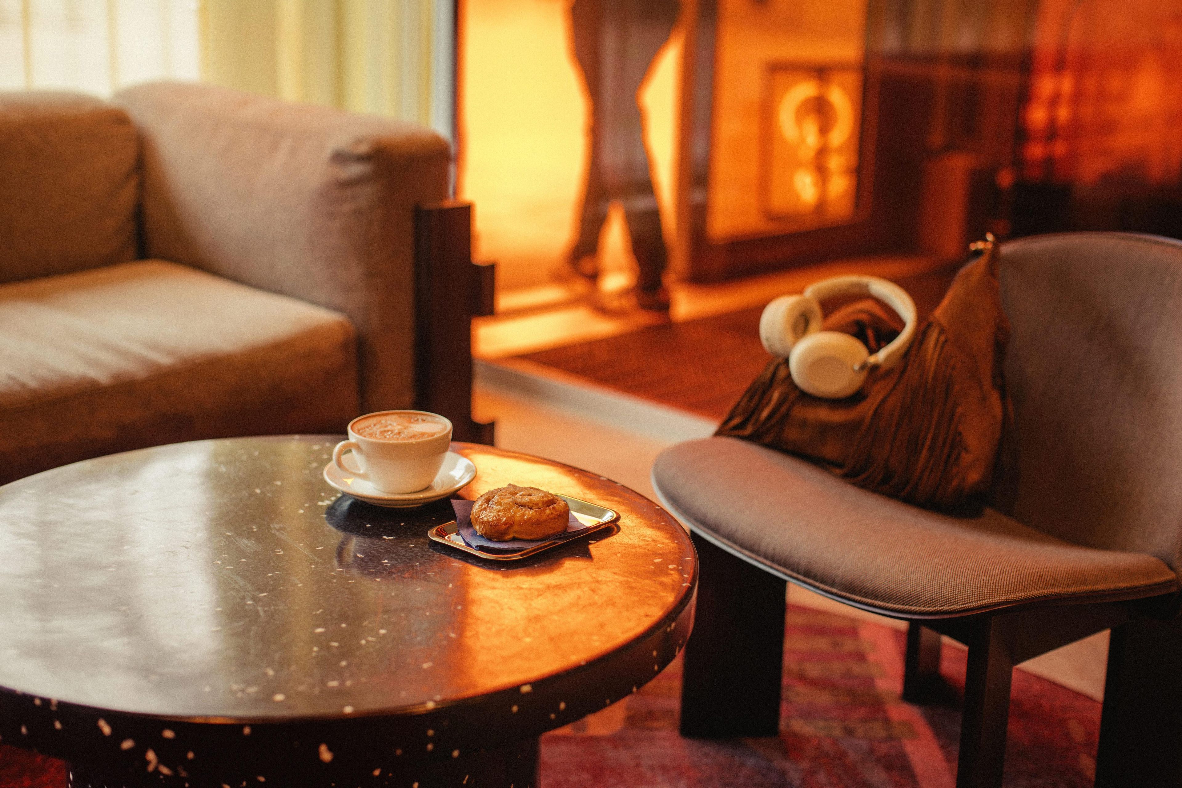 Un coin salon confortable avec une table ronde, une tasse de café, une pâtisserie et un casque posé sur une chaise.