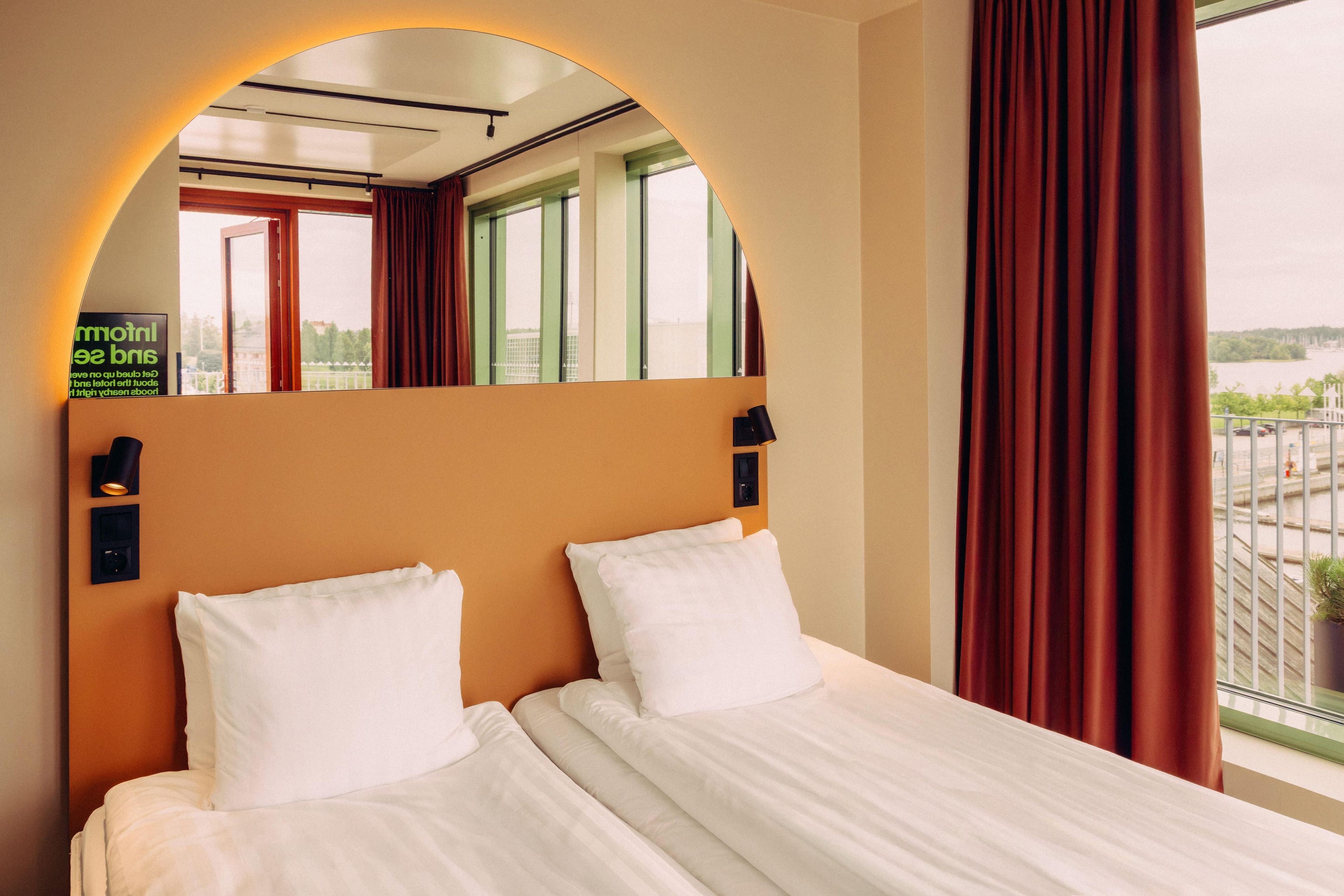 A hotel room with a bed, a mirror, and a view of the outside.