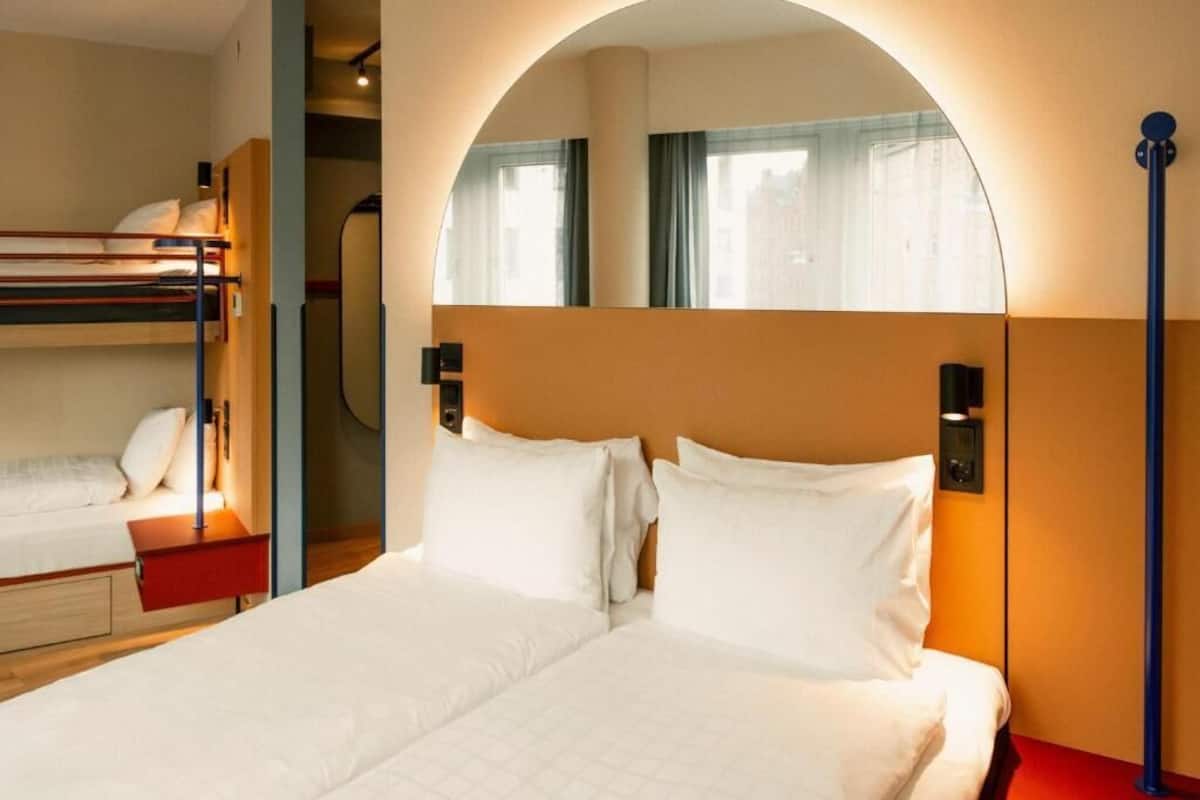 A hotel room with a bunk bed, a large mirror, and a red nightstand.