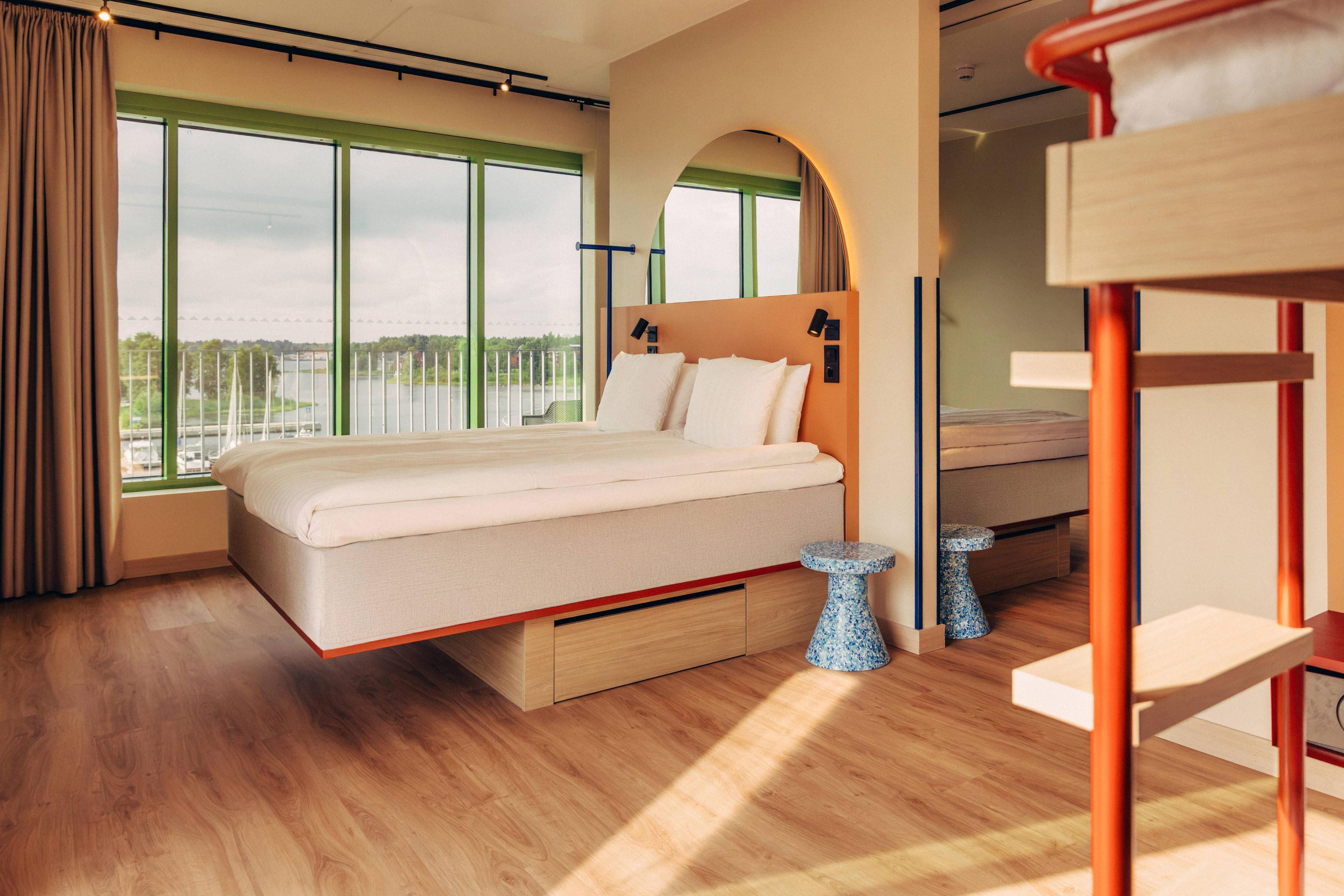 A modern bedroom with a large bed, a small table, and a view of a body of water through large windows.