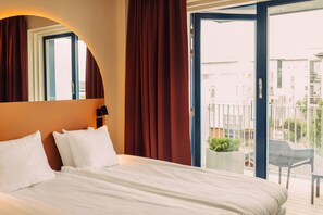Quarto de hotel com cama, janela com cortinas, varanda com cadeira e planta em vaso.
