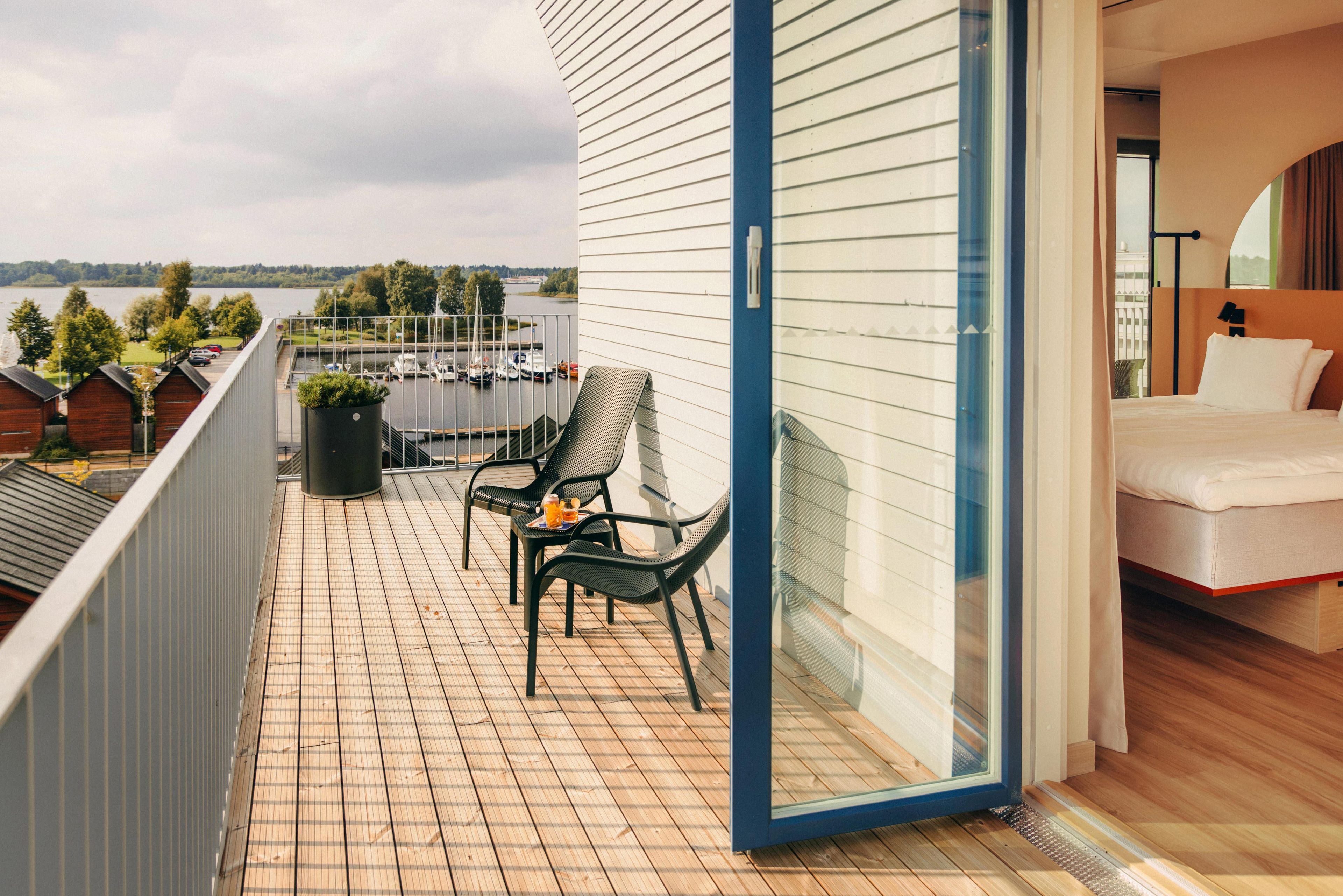 A balcony with a view of a body of water, a seating area with a table and chairs, and a bedroom with a bed and a window.