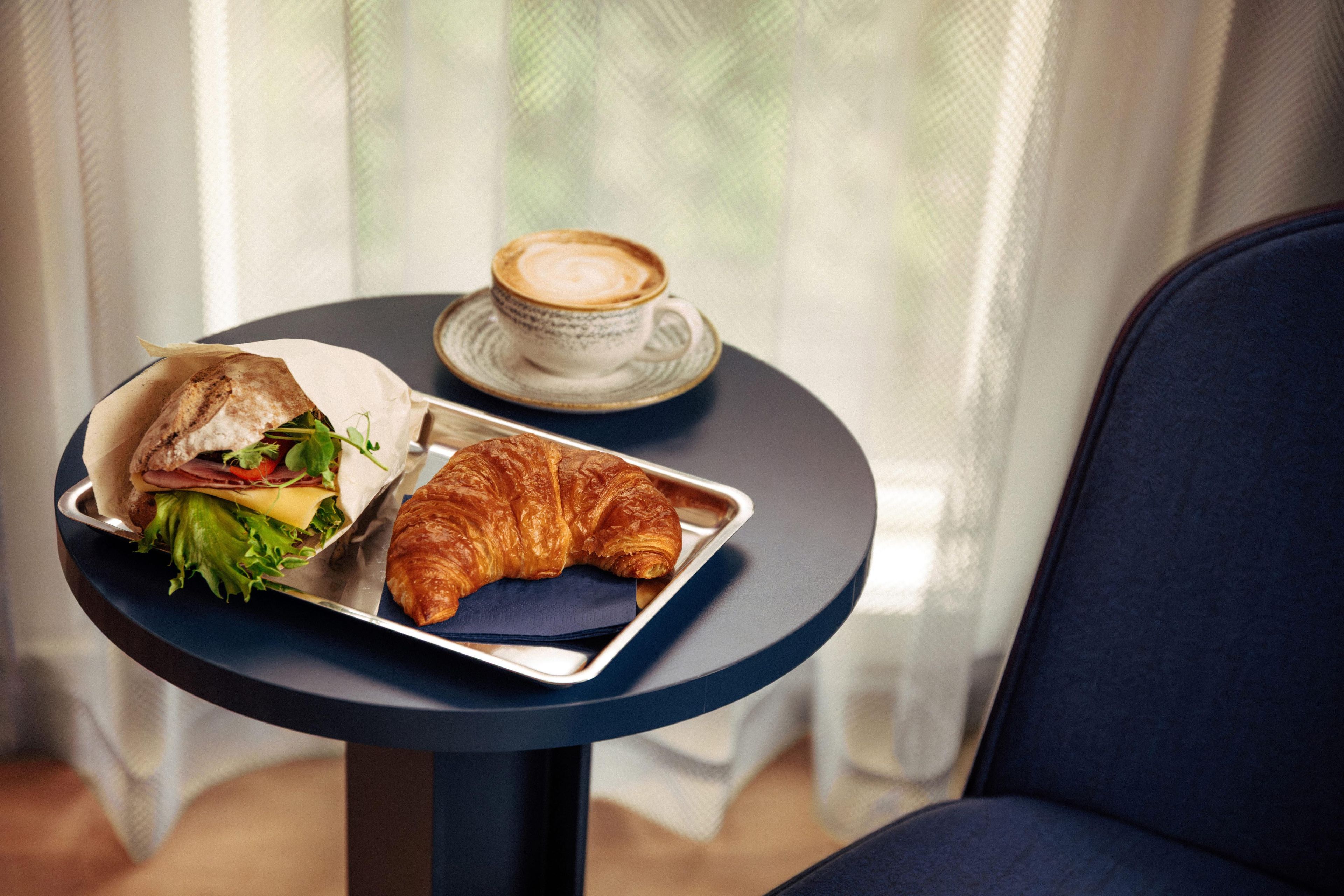 A table with a sandwich, a croissant, and a cup of coffee.