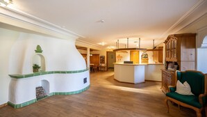 A spacious living area with a fireplace, wooden flooring, a green upholstered chair, and a kitchen area with wooden cabinets. - Urige Ferienwohnung Sammareier Gutshof in Bad Birnbach (Bad Birnbach)