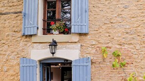 A stone building with a wooden door and blue shutters, a balcony with flowers, and potted plants outside. - The Cottage, Les Chouettes, Dordogne Valley where memories are made (Trémolat)
