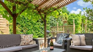 A covered patio area with wicker furniture, a table with a bottle and glasses, and a pergola overhead. - The Cottage, Les Chouettes, Dordogne Valley where memories are made (Trémolat)