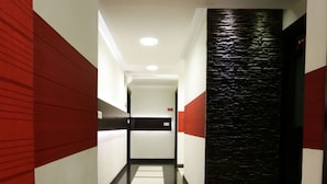 A modern hallway with a polished floor, red and white walls, and a textured black wall at the end. - Prajwal by Mango Hotels (Bengaluru)