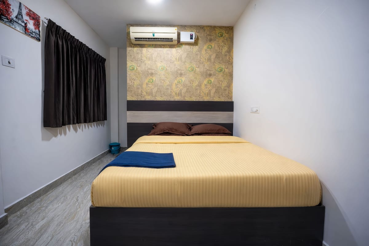 A bedroom with a bed, curtains, an air conditioner, and a wall with a decorative pattern.
