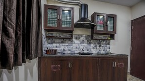 A kitchen with dark wooden cabinets, a black range hood, and a marble backsplash. - Rayzen Stays (Chennai)