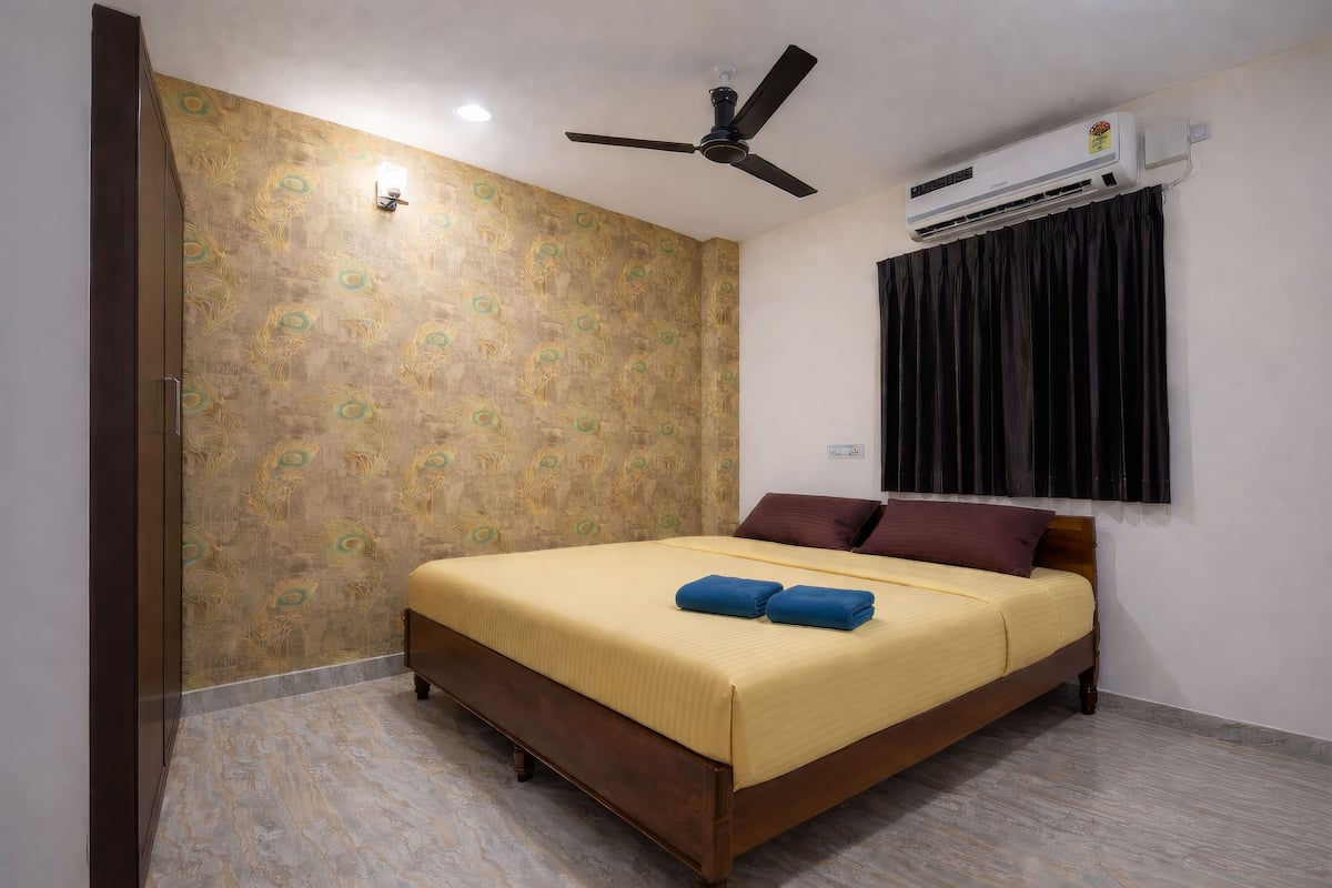 A bedroom with a bed, a ceiling fan, an air conditioning unit, and a window with curtains.
