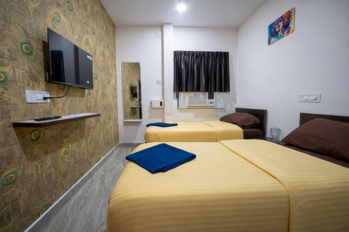 A hotel room with two beds, a TV mounted on the wall, a window with a curtain, and a painting on the wall.