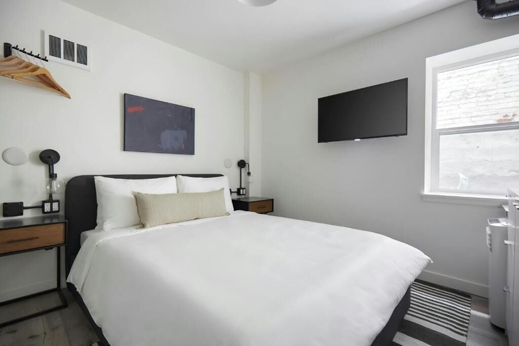 Une chambre d’hôtel moderne dotée d’un grand lit, d’un téléviseur à écran plat fixé au mur, d’une fenêtre offrant une vue agréable et d’un porte-manteau.
