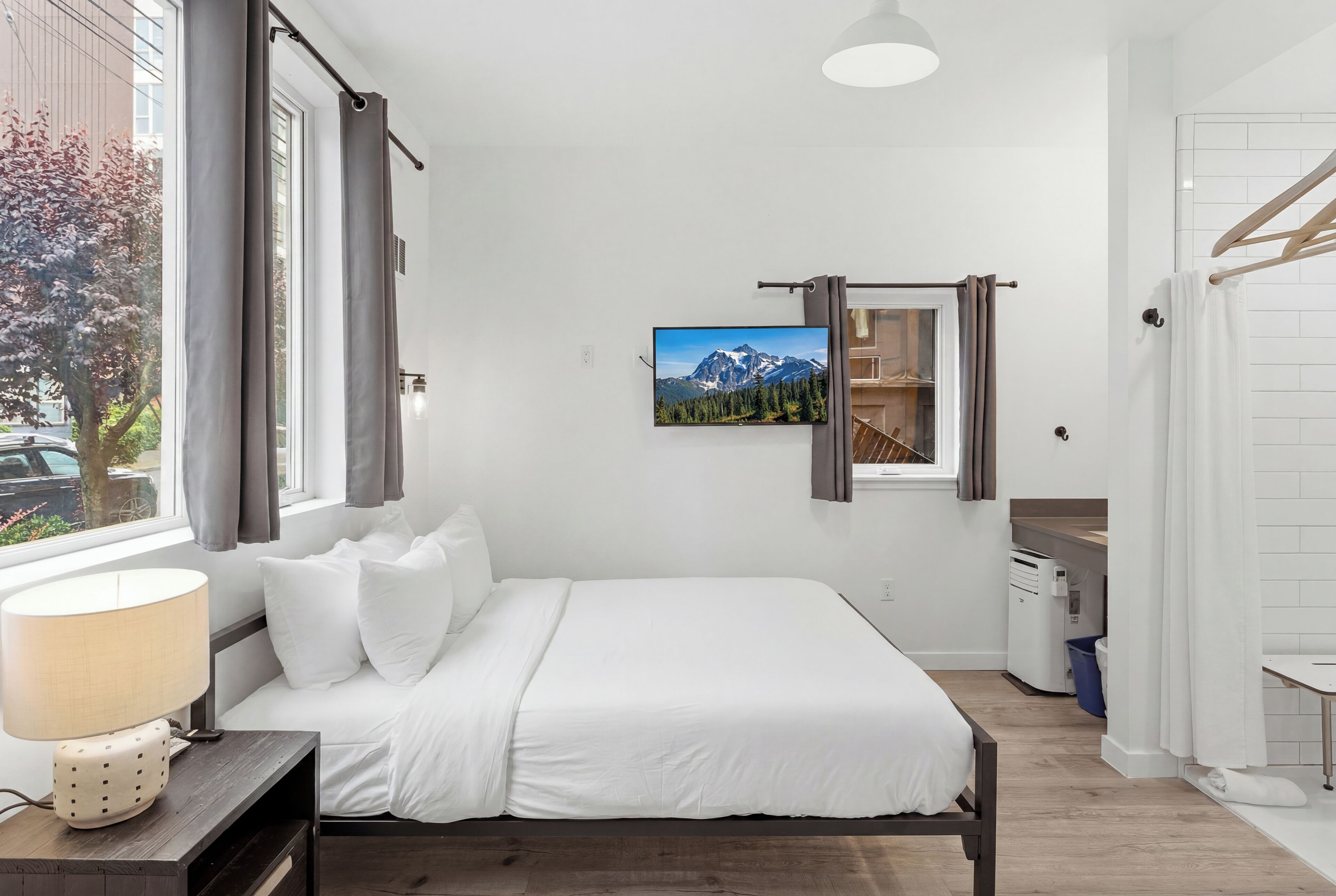A bedroom with a bed, a TV, a window with curtains, a lamp, and a view of mountains.