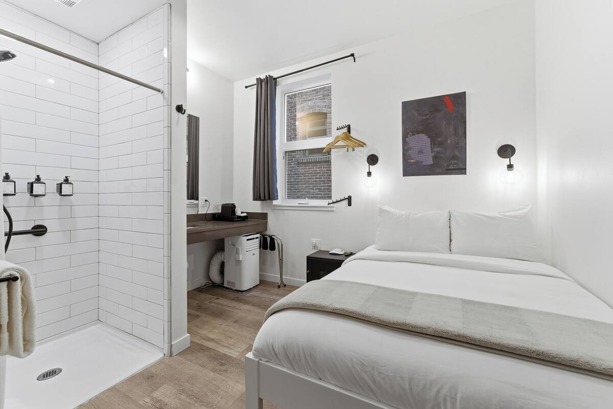 Une chambre d’hôtel moderne équipée d’une douche, d’un lit, d’un bureau et d’une fenêtre donnant sur un paysage agréable.