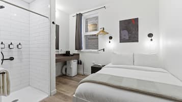 A modern hotel room with a shower, a bed, a desk, and a window with a view.