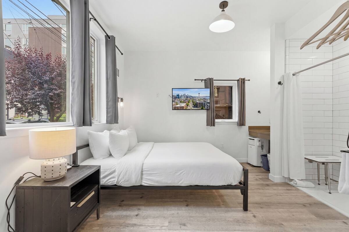 Une chambre à coucher moderne avec un lit, une table de chevet, une lampe et une vue sur le paysage urbain.