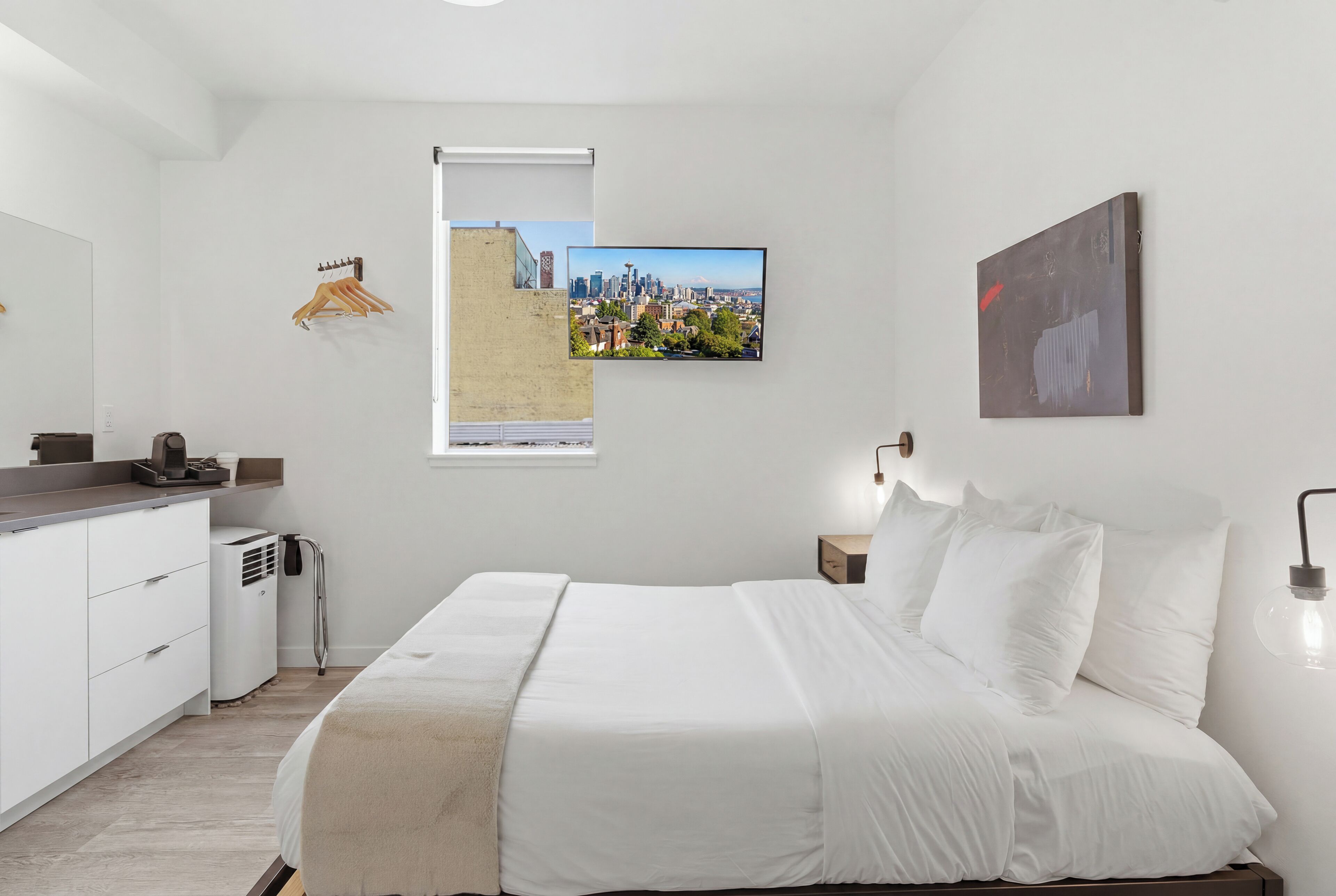 A modern bedroom with a bed, a cityscape view, a white dresser, and a heater.